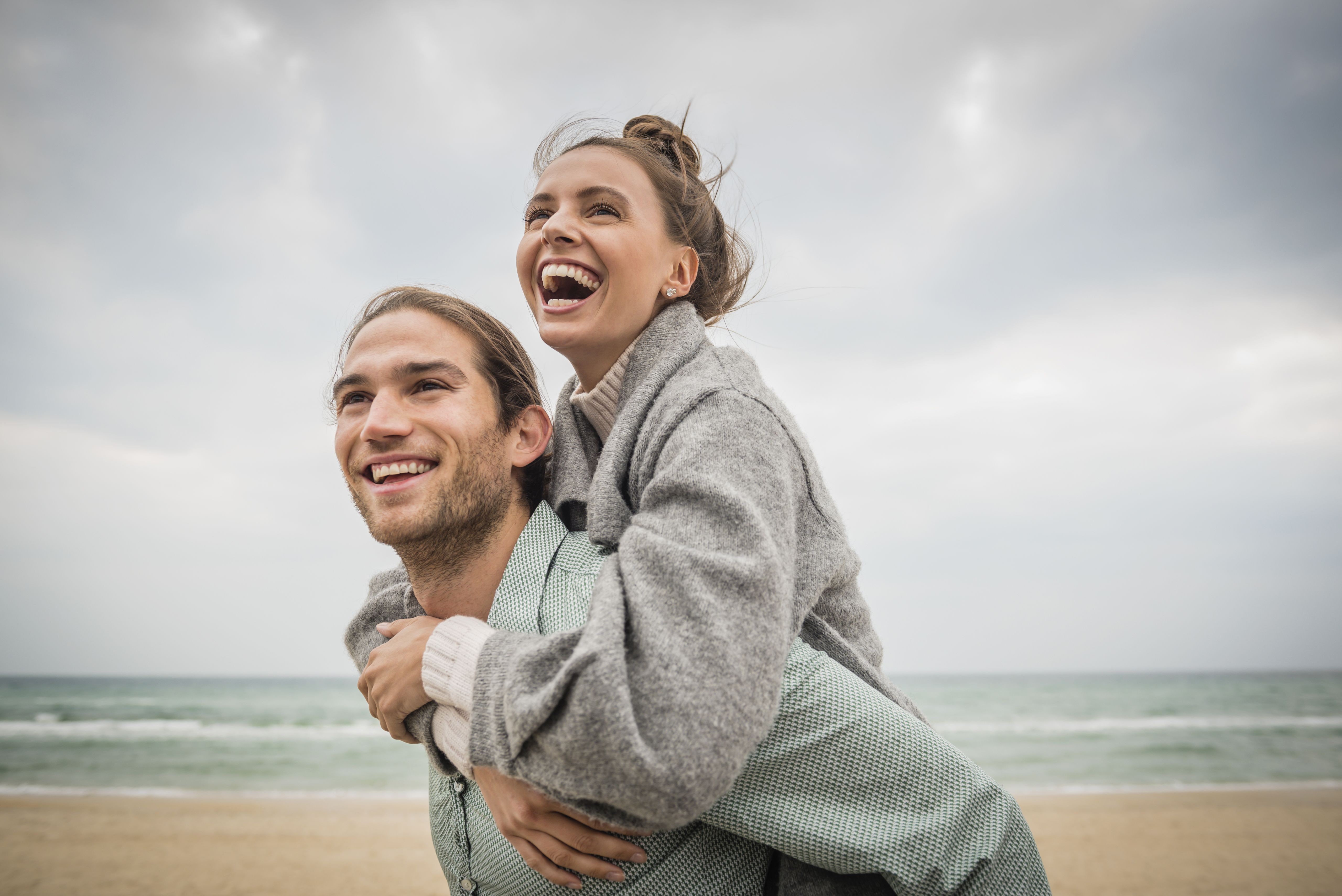Junges glückliches Paar an einem sonnigen Strand, der Mann trägt die Frau auf dem Rücken, was eine ernsthafte Begegnung, eine dauerhafte Beziehung und gemeinsame Momente veranschaulicht