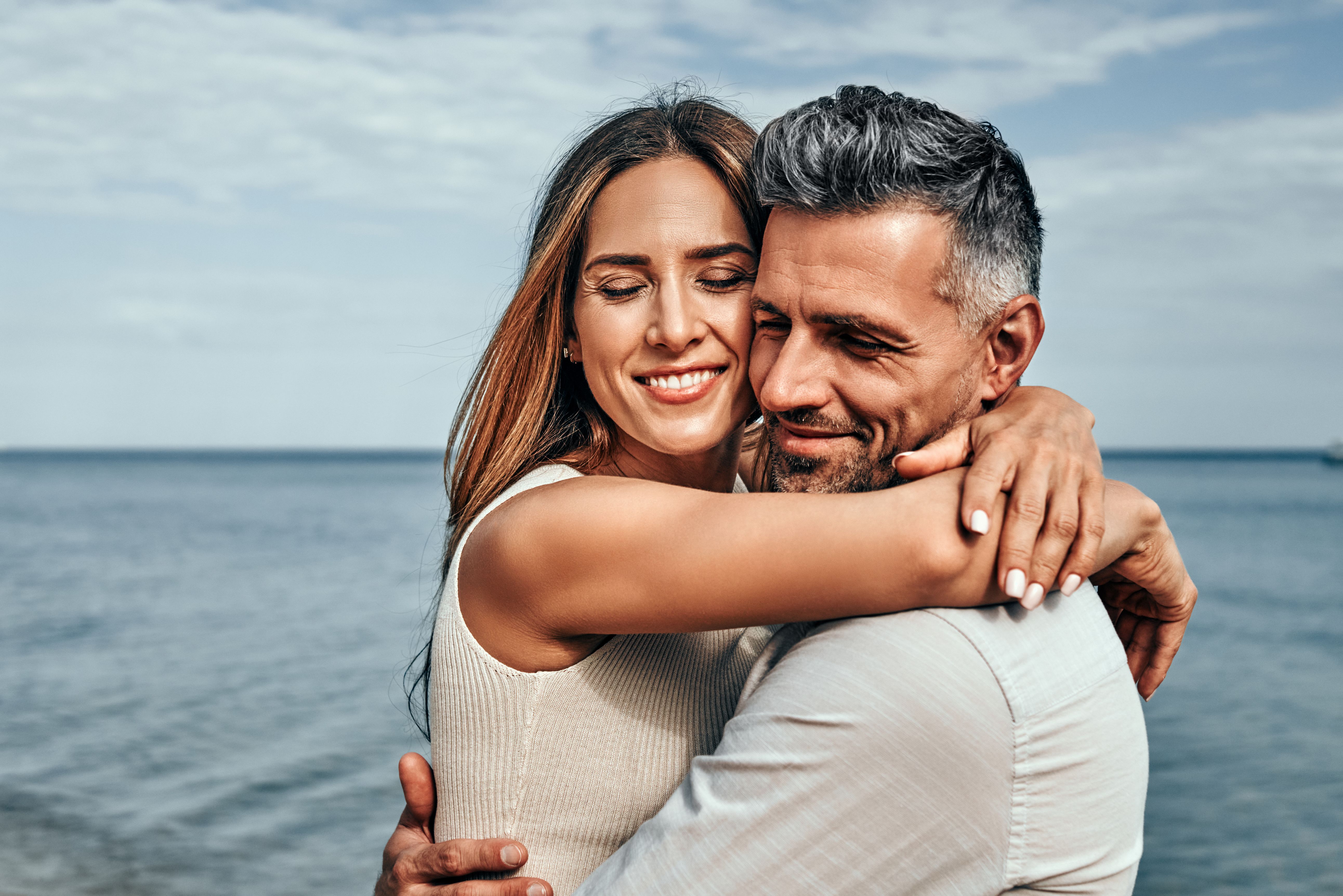 Paar in den Vierzigern, das sich im Sommer am Strand umarmt und eine ernsthafte Begegnung, eine dauerhafte Beziehung und Vertrauen zwischen Partnern veranschaulicht.