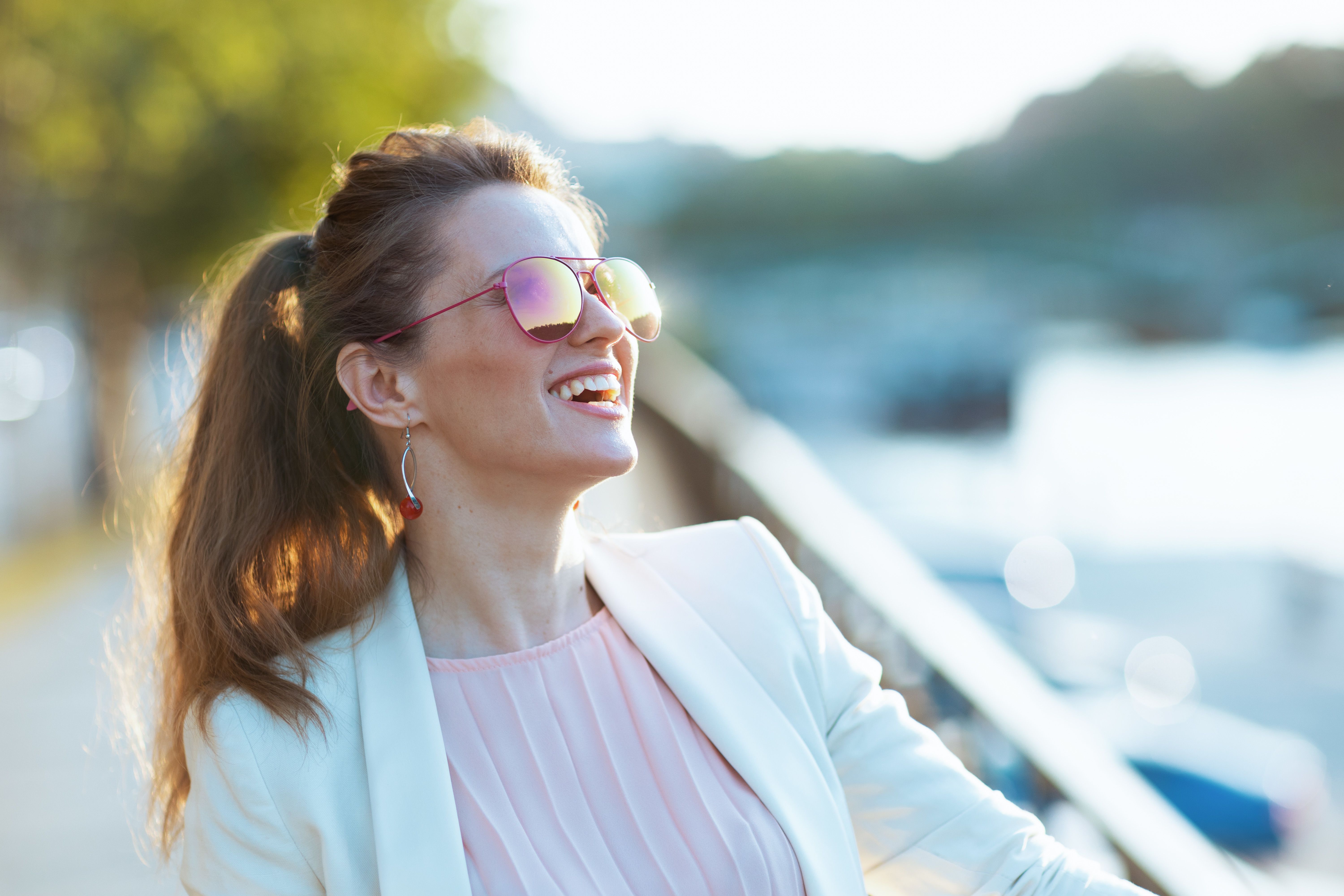 Lächelnde junge Frau mit Sonnenbrille, die in einem Café sitzt und auf ihr erstes Date nach einer Begegnung auf einer seriösen Partnerbörse wartet.
