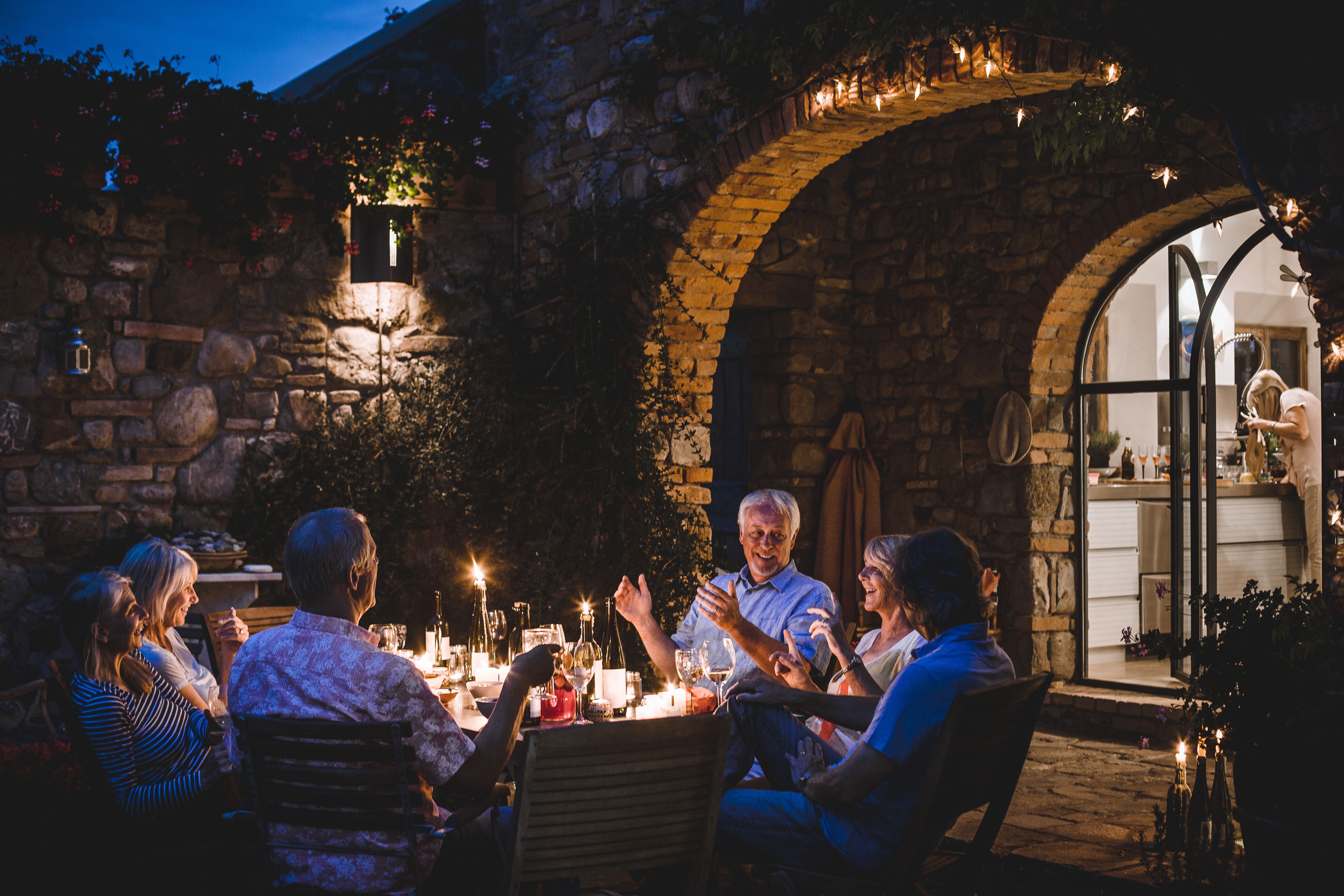 Lächelnde Freundesgruppe beim Abendessen im Garten, die einen Neuanfang, authentische Begegnungen und die Rückkehr ins soziale Leben nach einer Scheidung darstellt.
