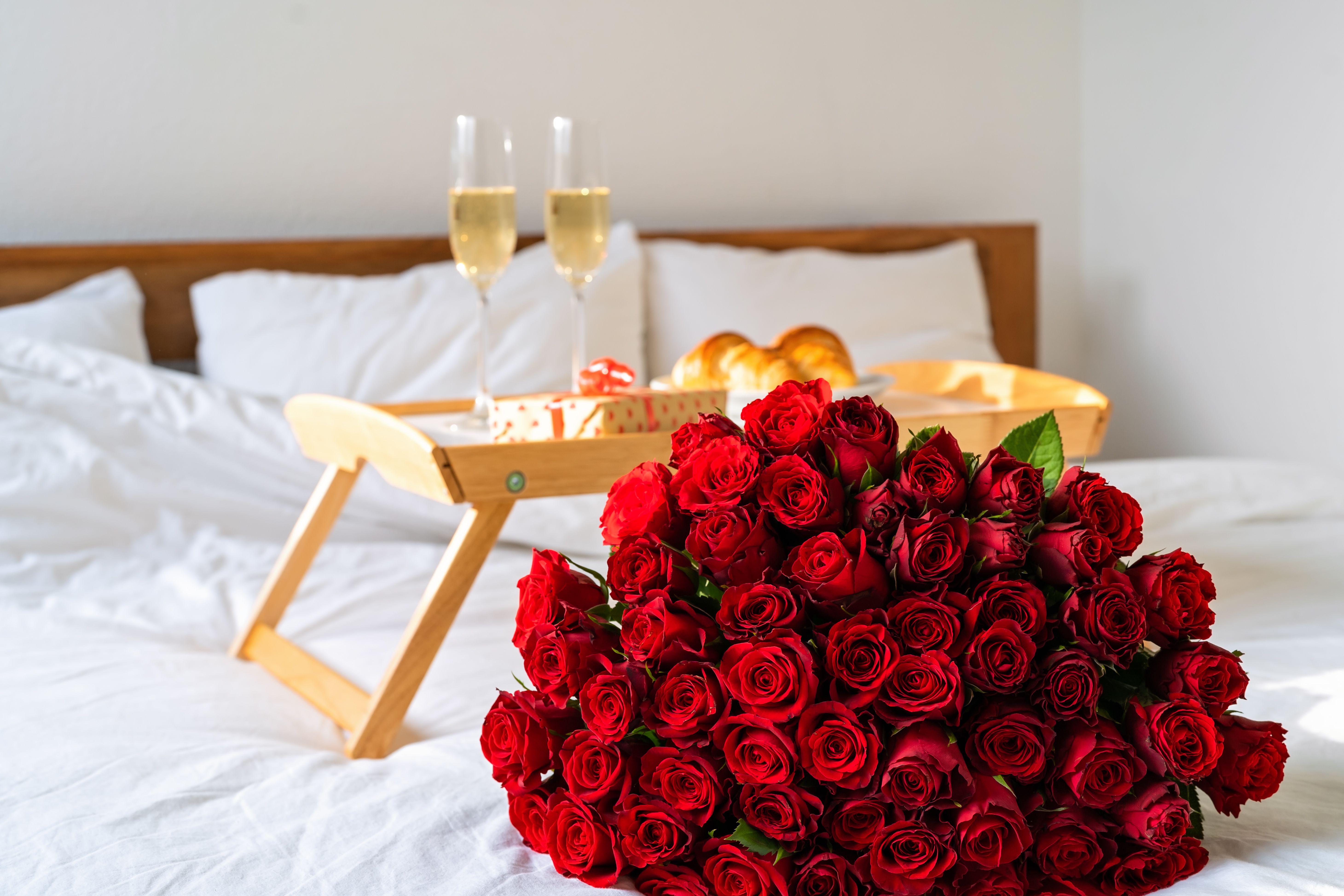 Großer Strauß roter Rosen auf einem Bett neben einem Frühstück für zwei.
