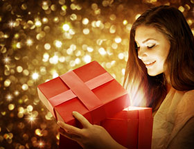 Frau betrachtet Geschenk vorm Weihnachtsbaum